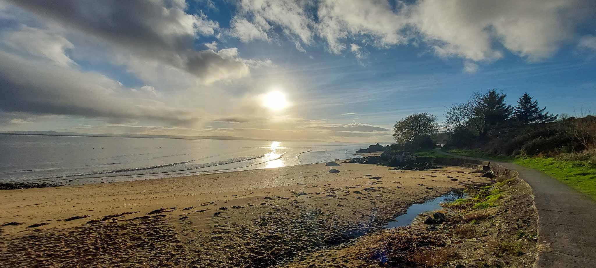 Low sunlight over Greencastle Beach, with a path following the shoreline
