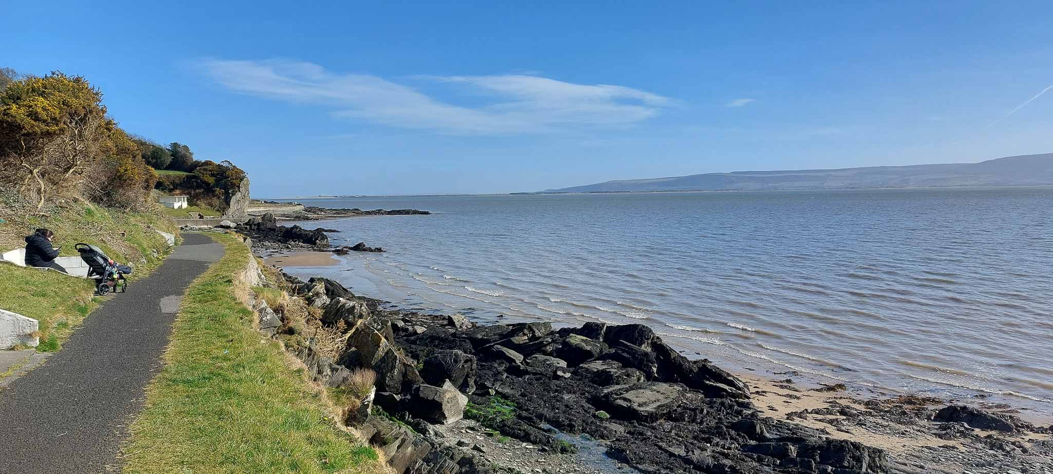 A path beside rocky beaches and a wide stretch of blue water
