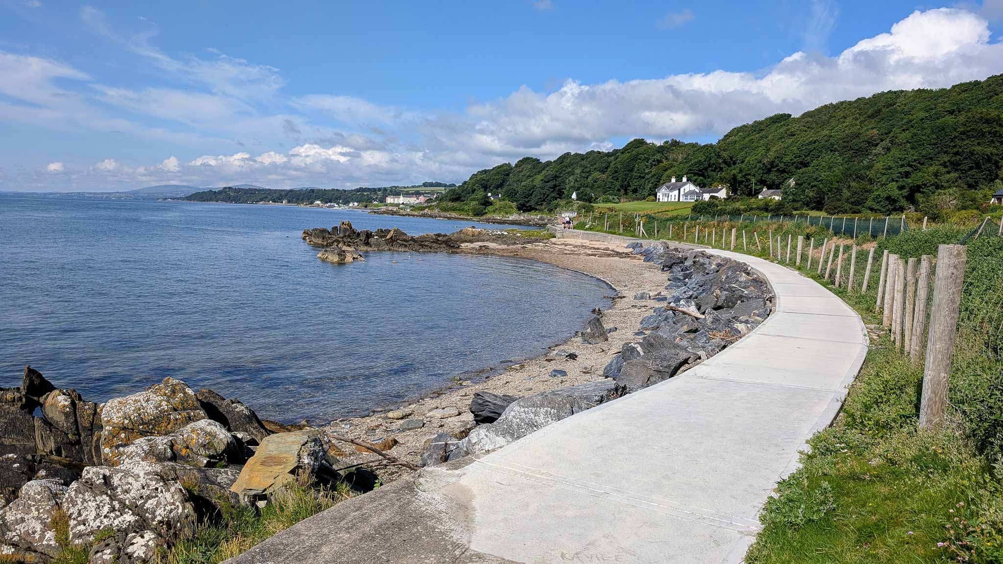 A winding coastal path beside calm water and rocky coves